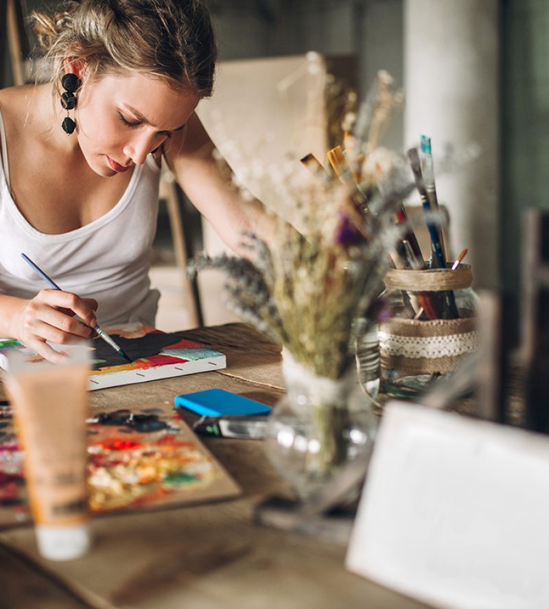 Beautiful young woman painting and drawing in her atelier - art studio