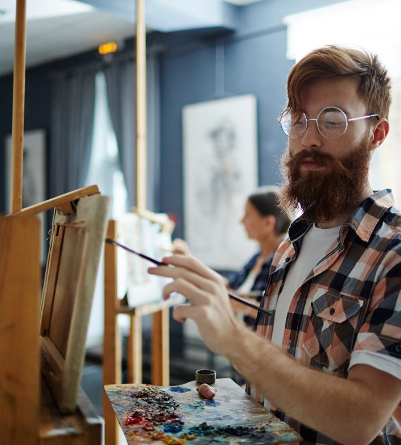 Skilled guy with palette painting something on easel